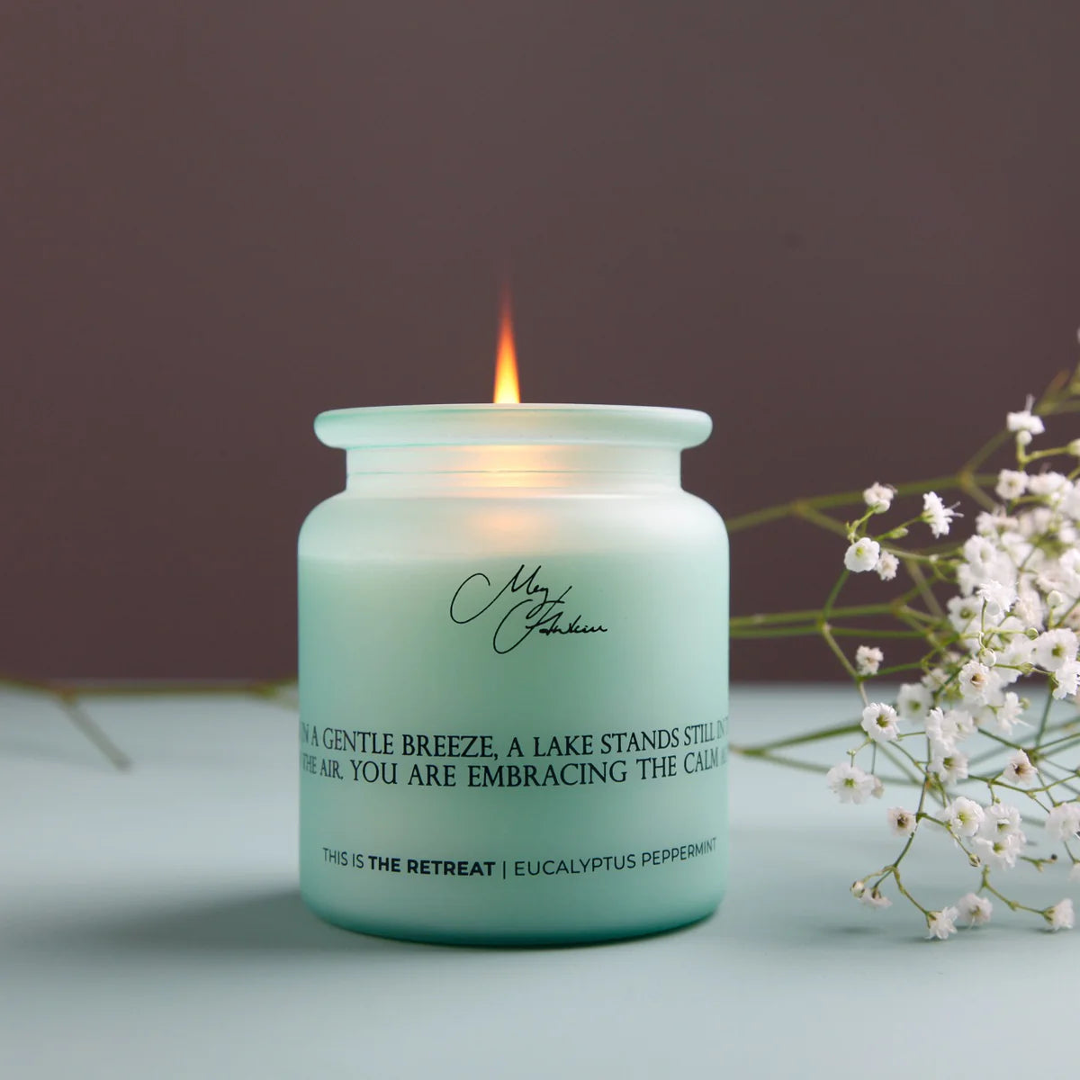 Lit candle in a green jar with text on a light surface and blurred background