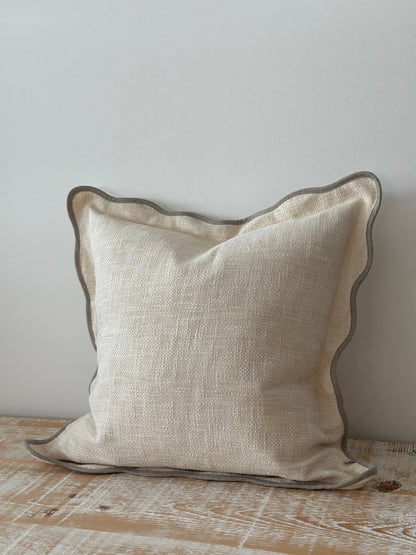 Beige pillow with brown trim on a wooden surface against a light gray wall
