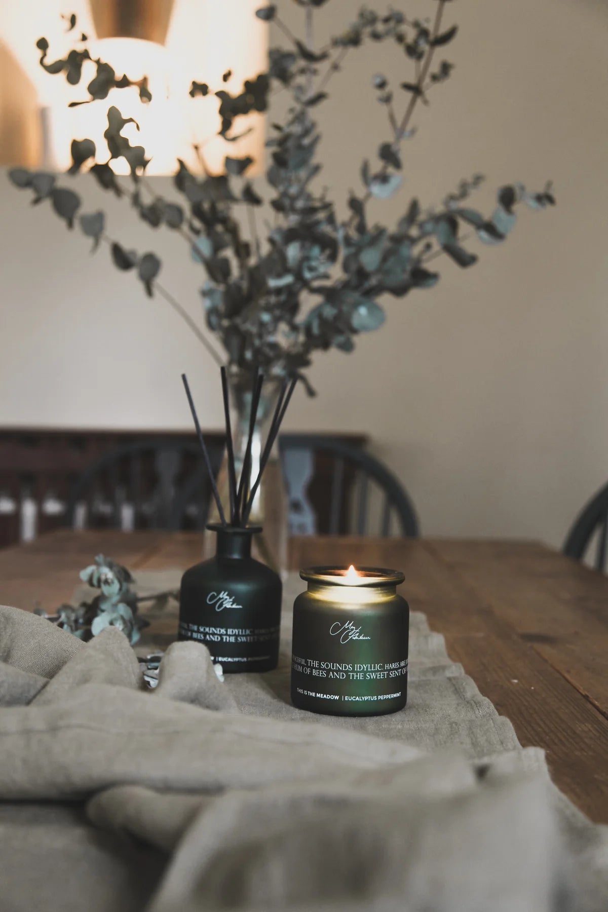 Dark green candle with decorative vase on a wooden table with blurred background
